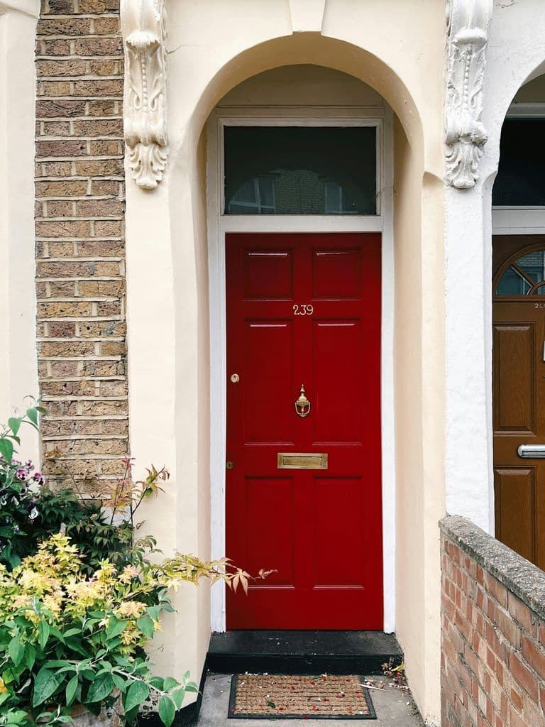 A quaint residential townhouse entrance with a vibrant red door and floral accents